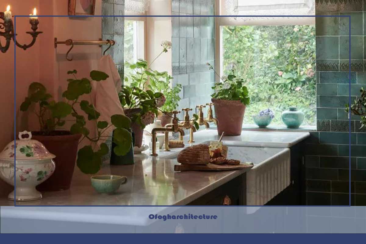 آشپزخانه به سبک کلبه‌ای با دیوارهای صورتی، پشتی سبز، سینک دوتایی با شیرهای برنجی، گیاهان، آویزهای اسکایپ